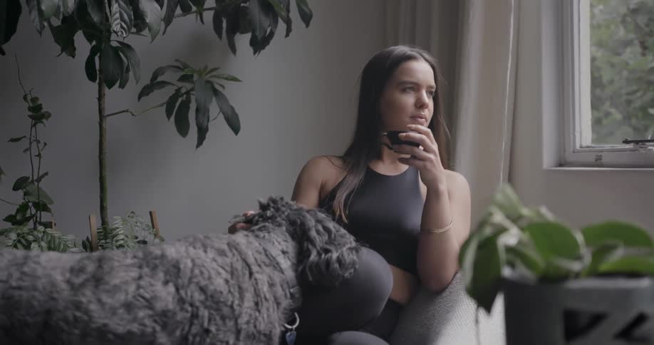 Woman sitting in chair in living room petting dog during the day