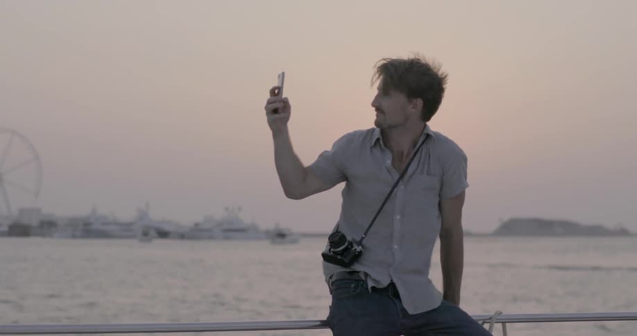 Man taking pictures with cell phone near ocean on windy evening