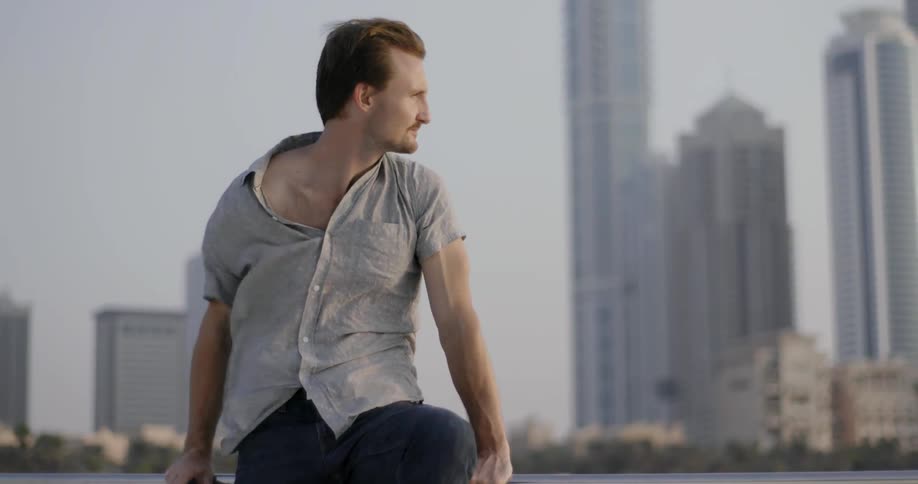Man sitting on a railing on a windy day with a city skyline in the background