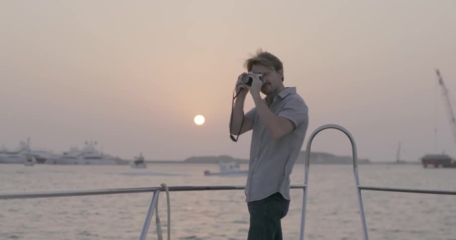A man takes photos from the bow of a boat at dusk