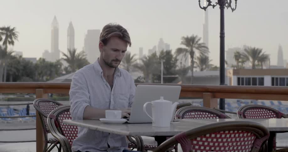 A man sips coffee on an outdoor patio in a city