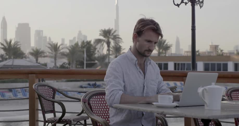 A man works on a laptop on a patio in a city