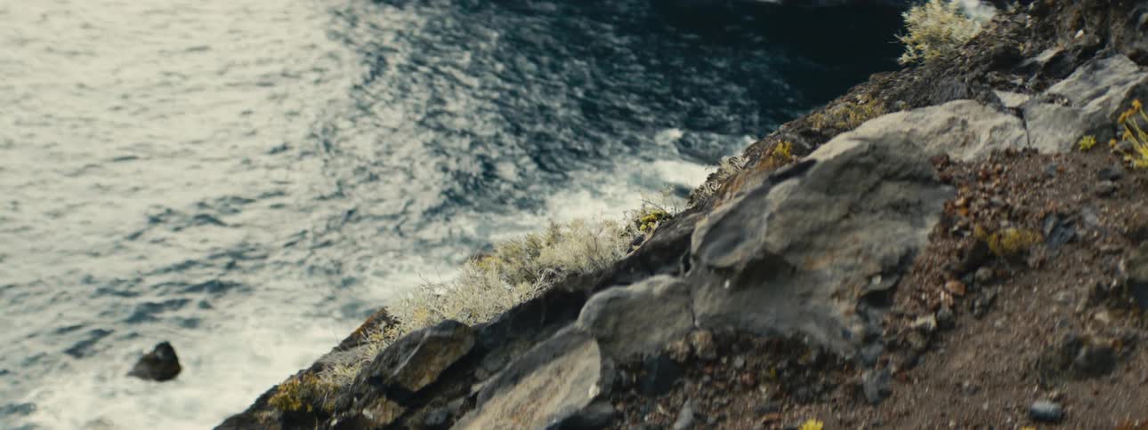 A high-angle view from a rocky cliff captures the turbulent motion of the ocean below