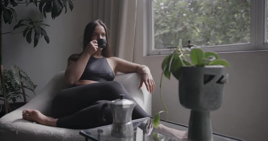 A young woman lounges in a living room chair sipping coffee