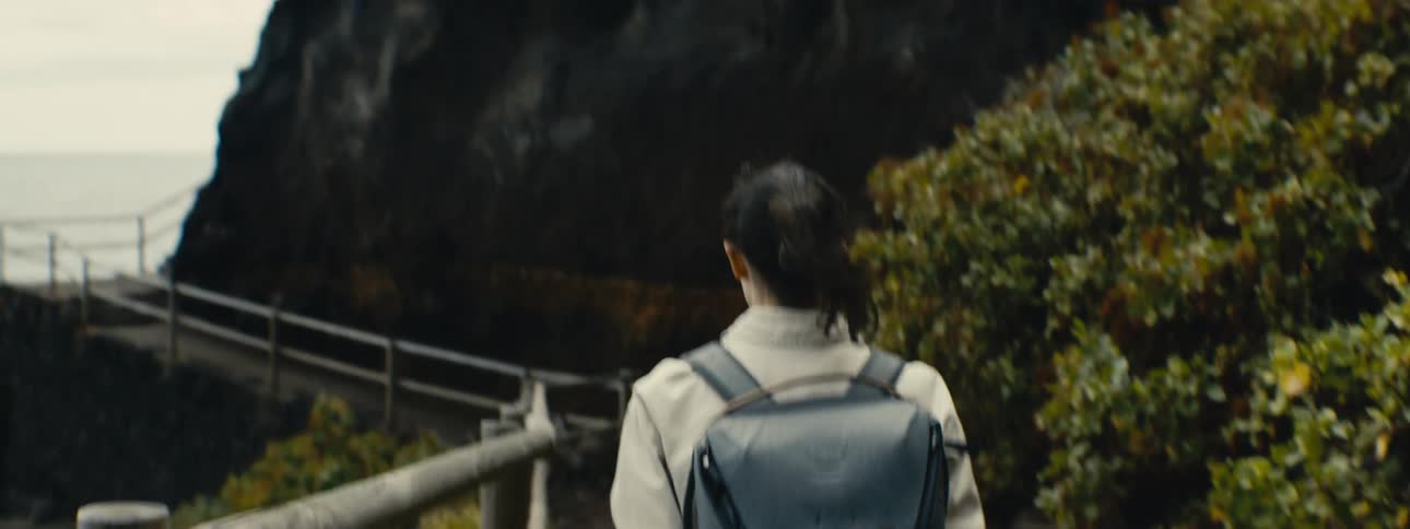 A female adventurer with a backpack explores a mountainous trail with a wooden boardwalk in slow motion