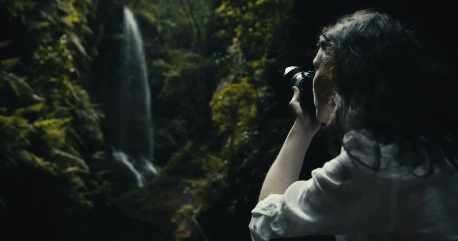 An adventurous female photographer captures a stunning waterfall hidden deep within a lush, green jungle