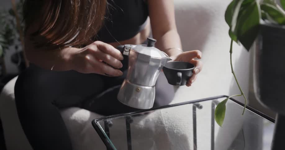 A woman pours a cup of coffee then leans back in her chair