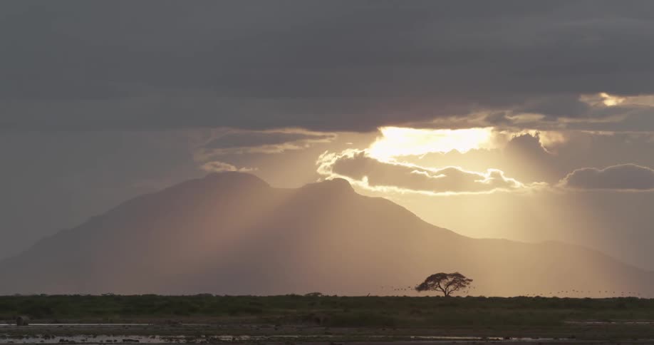 A view of the sun setting behind a mountain on cloudy day