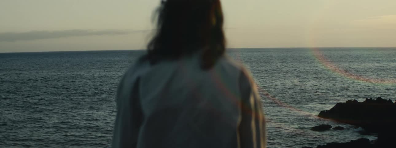 A person stands on a rocky coast, peacefully watching the serene ocean waves at sunrise