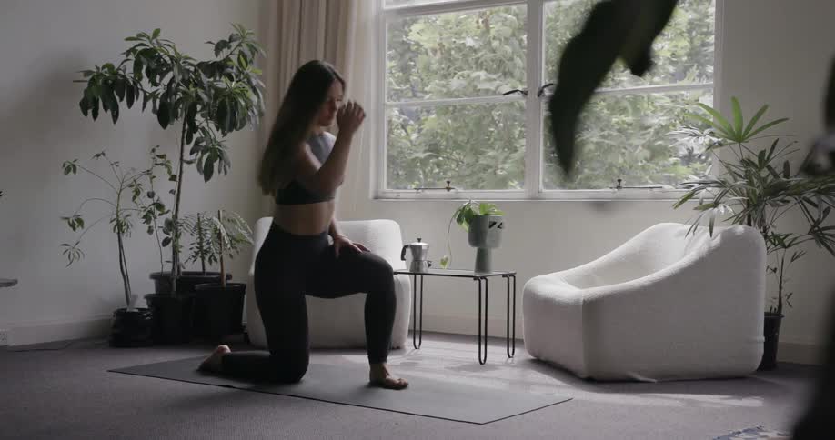 A woman kneels on a yoga mat and then stands