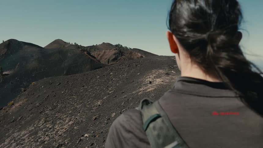 Slow motion over-the-shoulder shot of a female hiker with a backpack enjoying the windy view of a volcanic mountain range