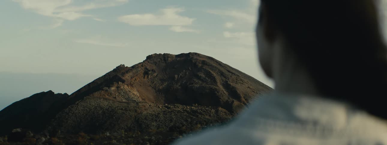 An over-the-shoulder view of a person looking out at a large, dormant volcanic mountain
