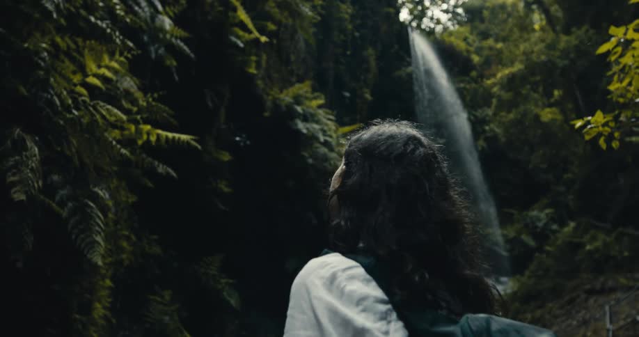 A traveler pauses to admire a magnificent waterfall cascading down a verdant cliff in a secluded rainforest