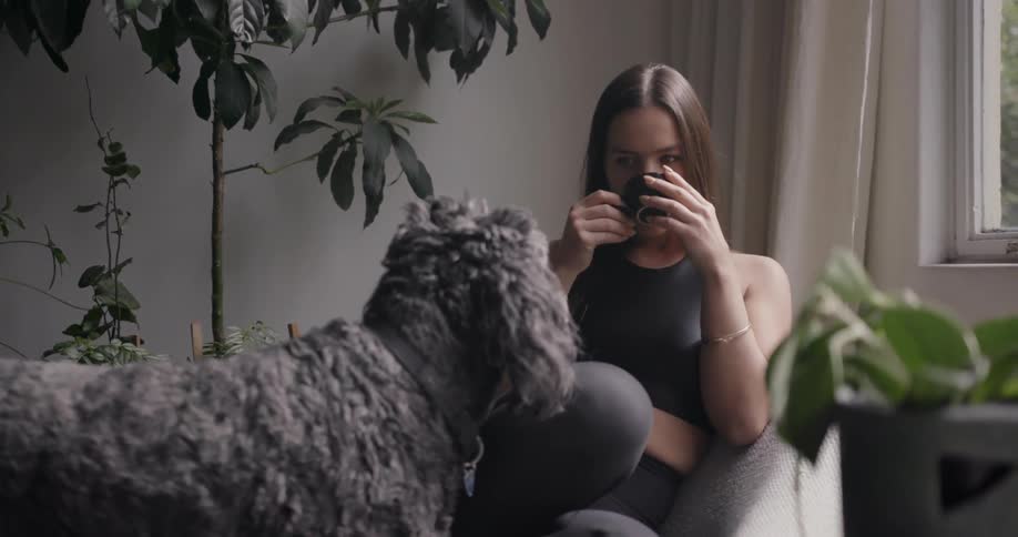 Woman drinks out of a tea cup with a dog on her lap