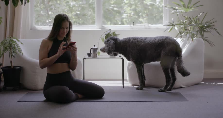 A woman with a dog beside her sits on the floor looking at her phone