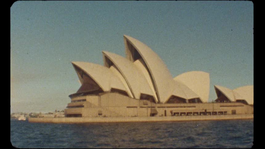 A vintage, grainy film shot captures the iconic Sydney Opera House from the shimmering water on a clear day