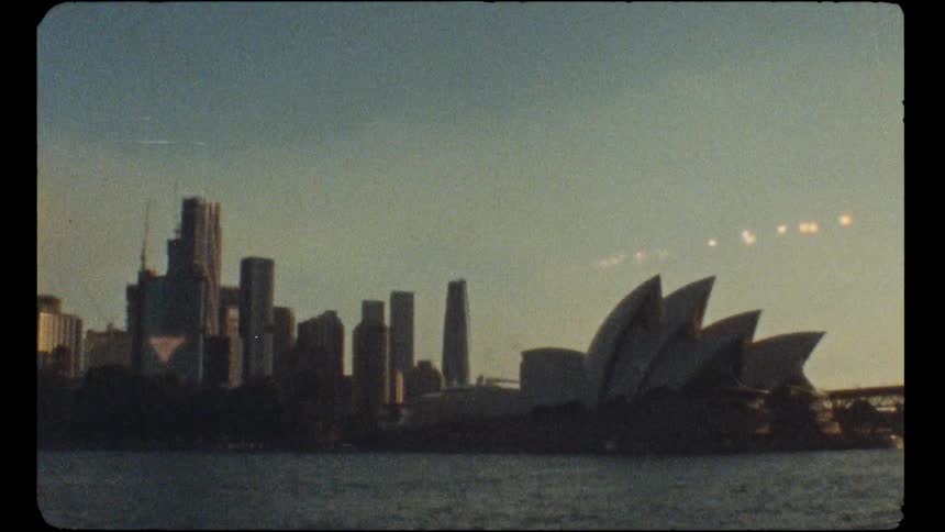 Vintage archival footage of the Sydney Opera House and city skyline from across the harbor at sunset
