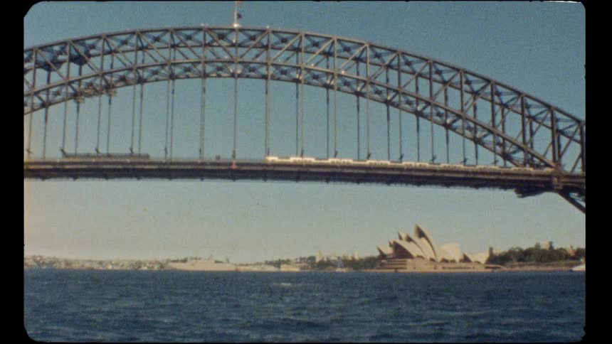 Vintage film captures a classic view of the Sydney Harbour Bridge with the Opera House in the background on a sunny day