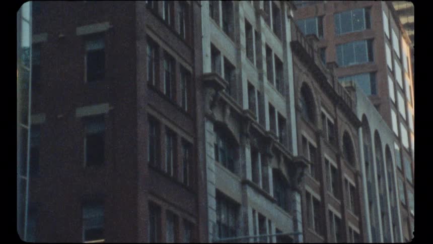 A vintage film shot tilts up the facade of a classic brick building to reveal modern skyscrapers in a downtown city setting