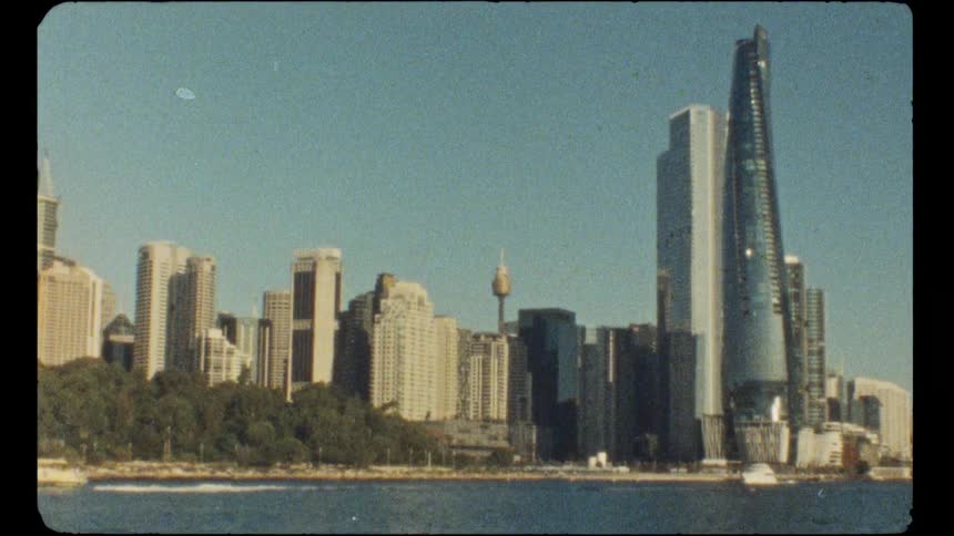 A vintage, film-grain view of the sunny Sydney skyline as seen from a boat on the harbor