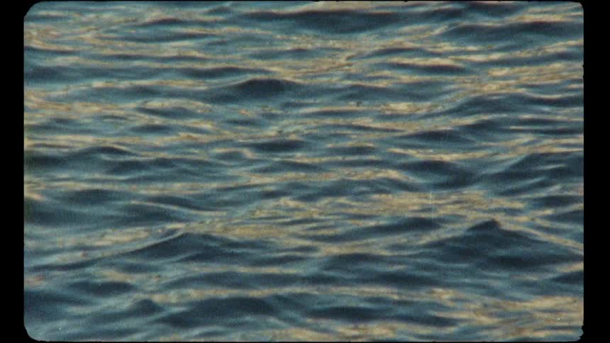 Gentle blue ocean waves with golden reflections create a serene and peaceful scene in a vintage Super 8 clip