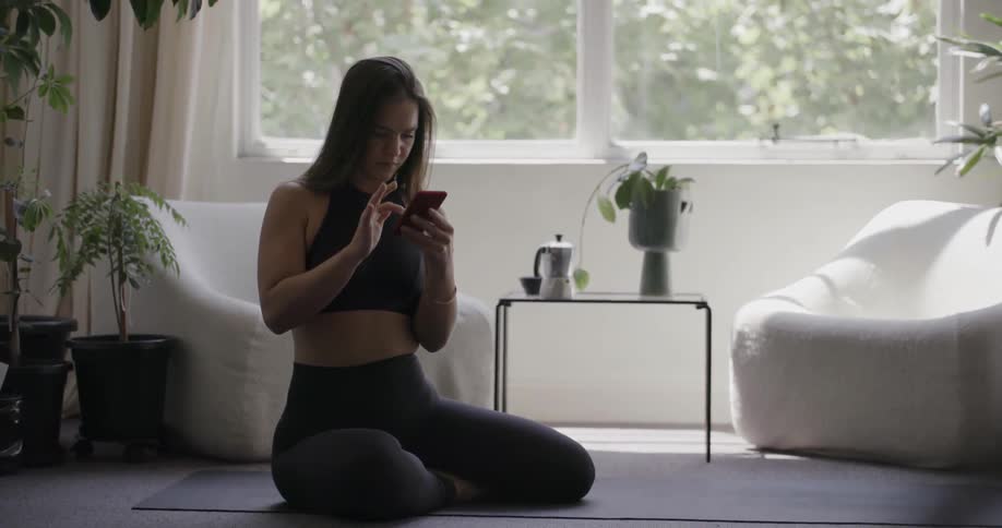 Woman sits on a yoga mat looking at a phone