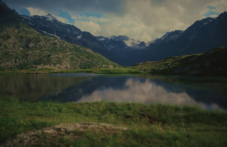 A picturesque alpine lake perfectly reflects the surrounding snow-capped mountains and cloudy sky