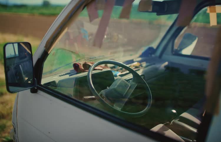 The rustic interior of an old white work van parked in the sunny countryside