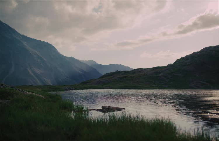 Sunlight filters through clouds to illuminate a peaceful mountain landscape with a calm lake in the foreground