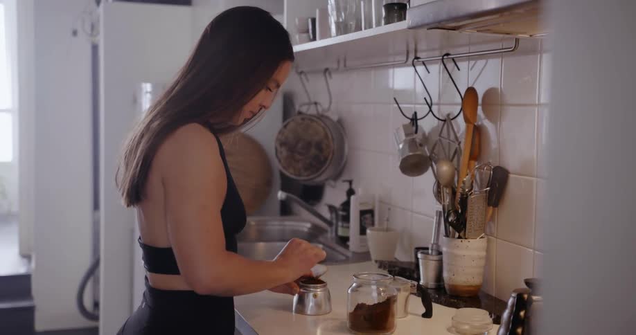 A dog walks into a kitchen while a woman scoops coffee grounds