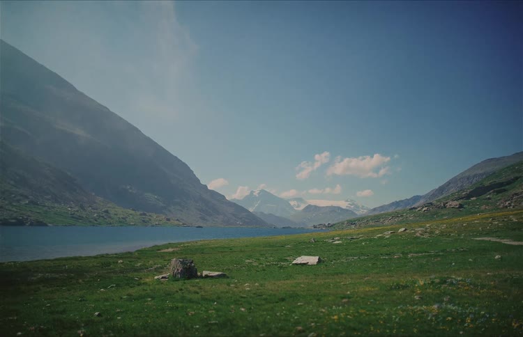 A serene wide shot of a tranquil alpine lake nestled in a lush green valley between majestic mountains
