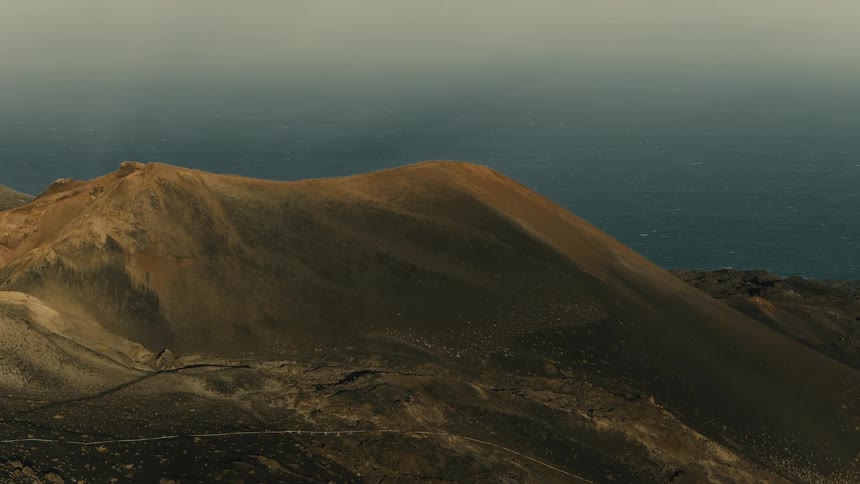 Slow aerial pull-back reveals a vast volcanic crater and a distant lighthouse overlooking the expansive ocean