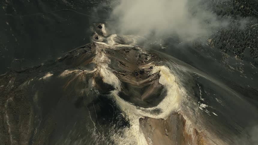 A powerful high-angle aerial view shows a desolate volcanic crater emitting a plume of steam