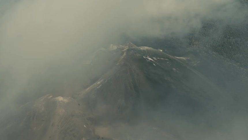 Aerial view of thick smoke and gas clouds clearing to reveal the volcanic craters of Mount Etna