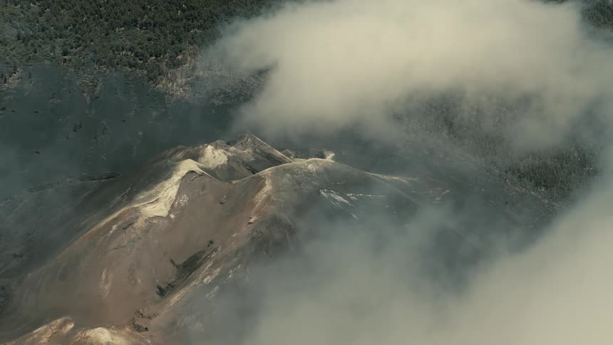 A stunning aerial view of a smoking volcanic crater as clouds roll over the rocky, desolate landscape