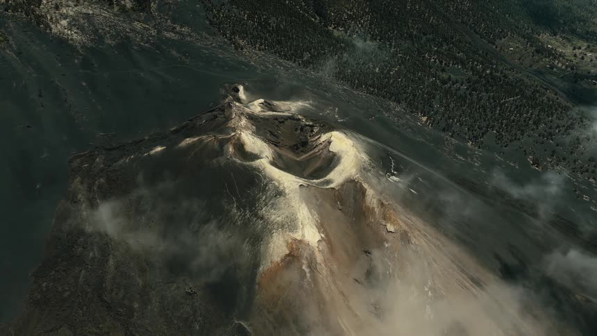 A dramatic aerial view pulls back to reveal the immense scale of a steaming volcanic crater and its dark, ashen slopes