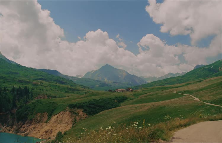 A majestic and serene wide shot of a lush green mountain valley with a winding road under a cloudy blue sky
