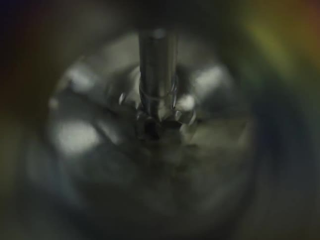 A close-up, high-speed view from above as a mechanical mixer blends a liquid in a metal container