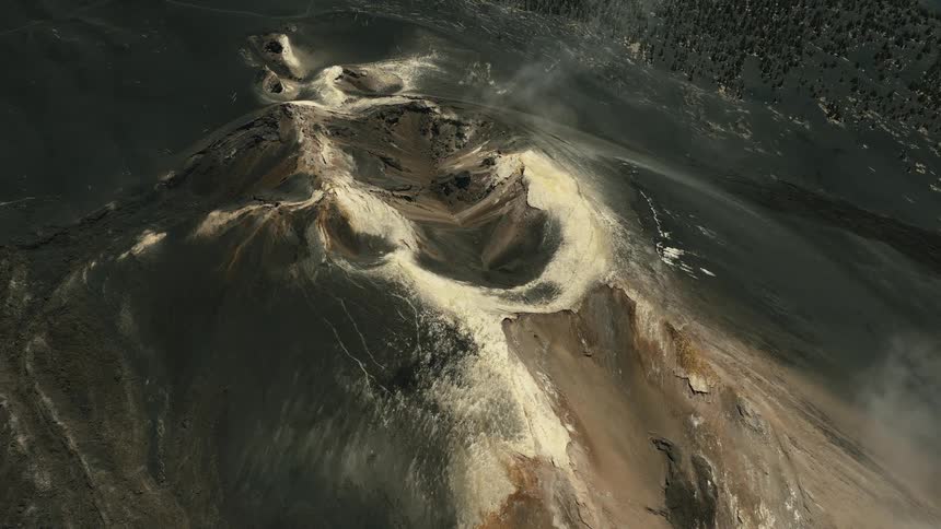 A dramatic high-angle aerial view of a desolate volcanic crater with steam rising as the camera slowly pulls back