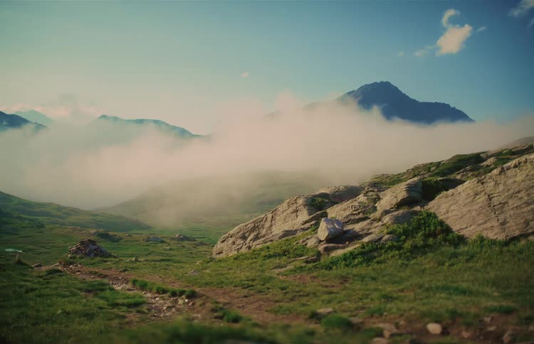 Misty clouds move through a green mountain valley with a dreamy, vintage light leak effect