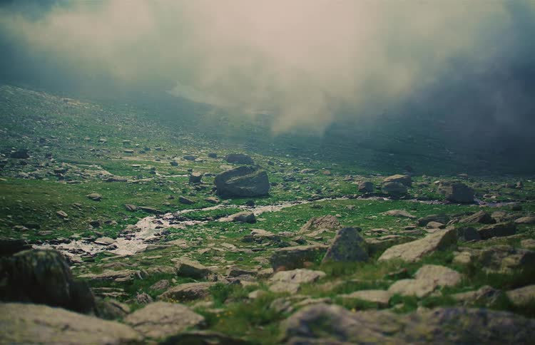 Ethereal fog rolls over a serene, rocky mountain landscape with a flowing creek