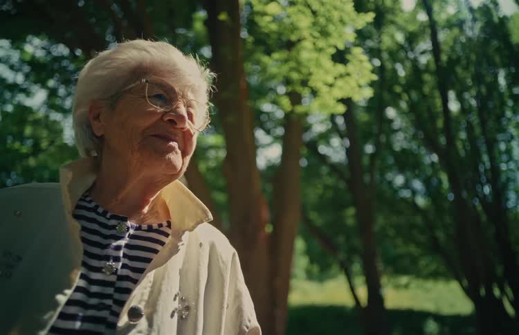 A serene elderly woman smiles warmly while enjoying a sunny day outdoors in a lush green park