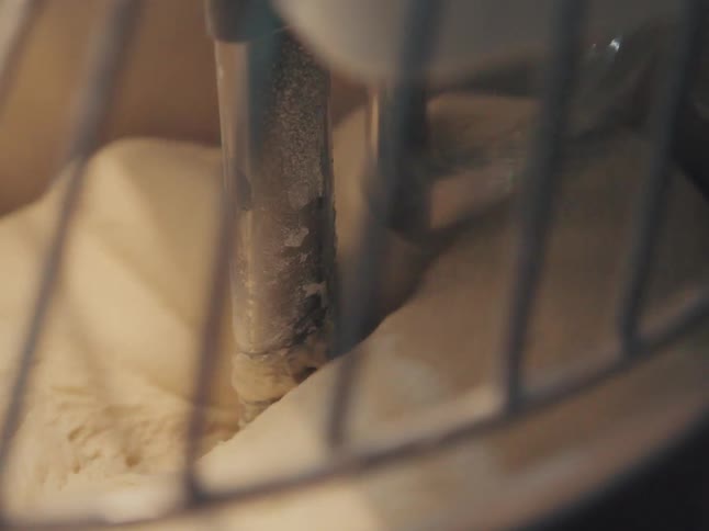 A close-up shot of an industrial spiral mixer kneading a large batch of bread dough inside a professional bakery