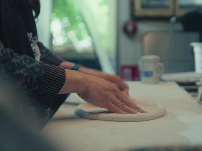 A looping close-up shot shows a baker's hands rhythmically kneading and shaping pizza dough on a floured kitchen counter