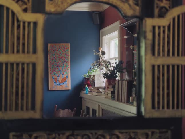 An ornate antique mirror with open shutters reveals the reflection of a quiet, artfully decorated room
