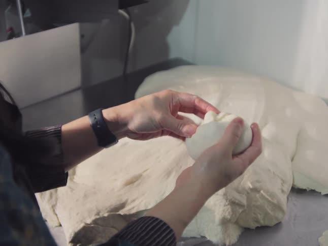 Close up of a baker's hands skillfully shaping a ball of fresh dough on a stainless steel counter in a professional kitchen