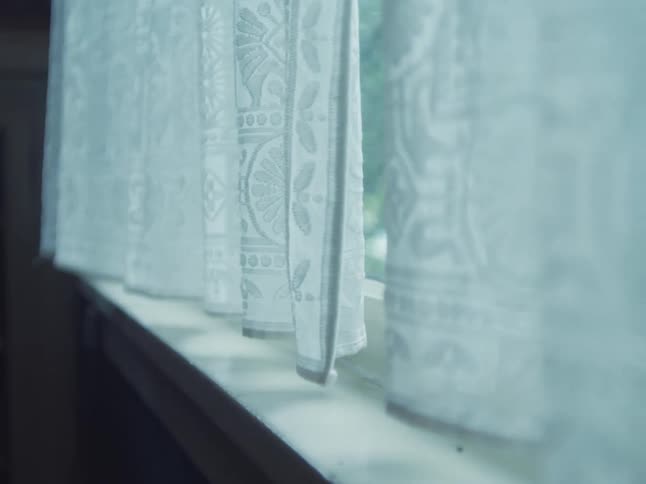 Soft daylight filters through delicate white lace curtains hanging in a window, gently moving in a subtle breeze