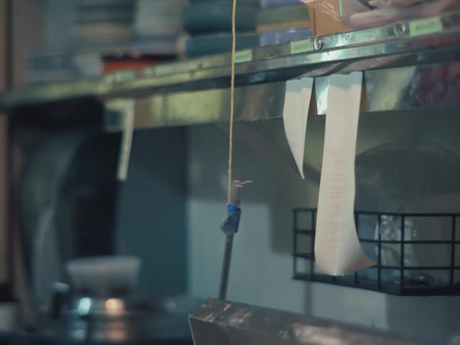 A close-up of restaurant order tickets hanging on a metal shelf in a commercial kitchen