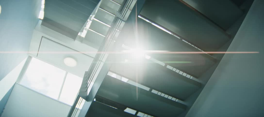 Low angle shot of a person walking down a modern staircase as bright sunlight creates a beautiful lens flare