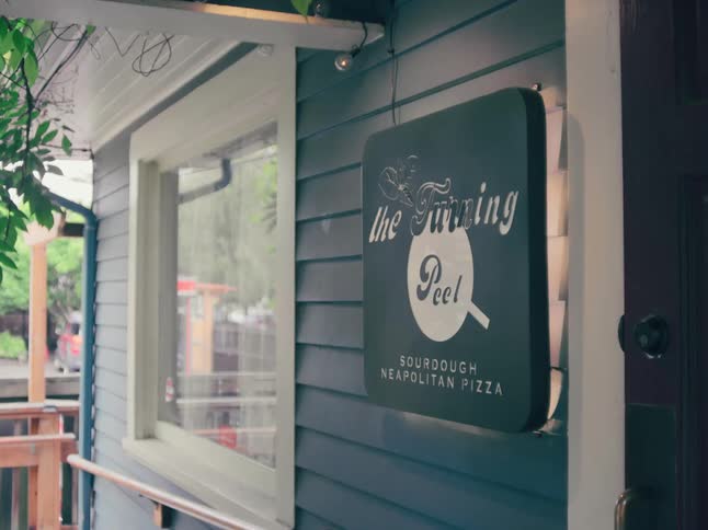 A stylish sign for a Sourdough Neapolitan Pizza restaurant called 'the Turning Peel' hangs on the exterior of the building